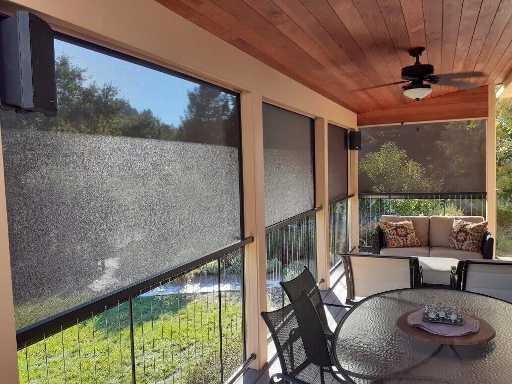 Outdoor patio with solar shades, seating area, and greenery visible through the screens.