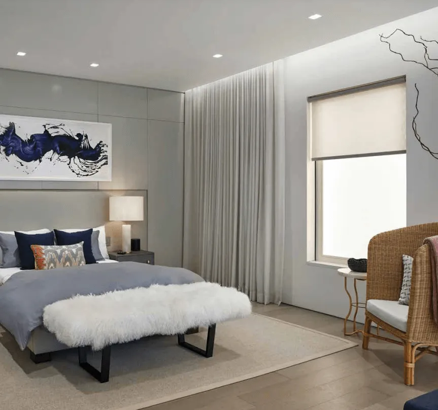Modern bedroom with blue and white decor, a fur bench, and large window.