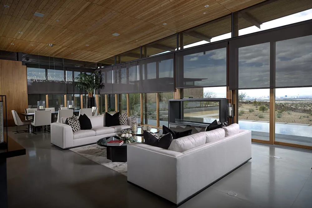 Modern living room with large windows, sleek sofas, and roller shades.