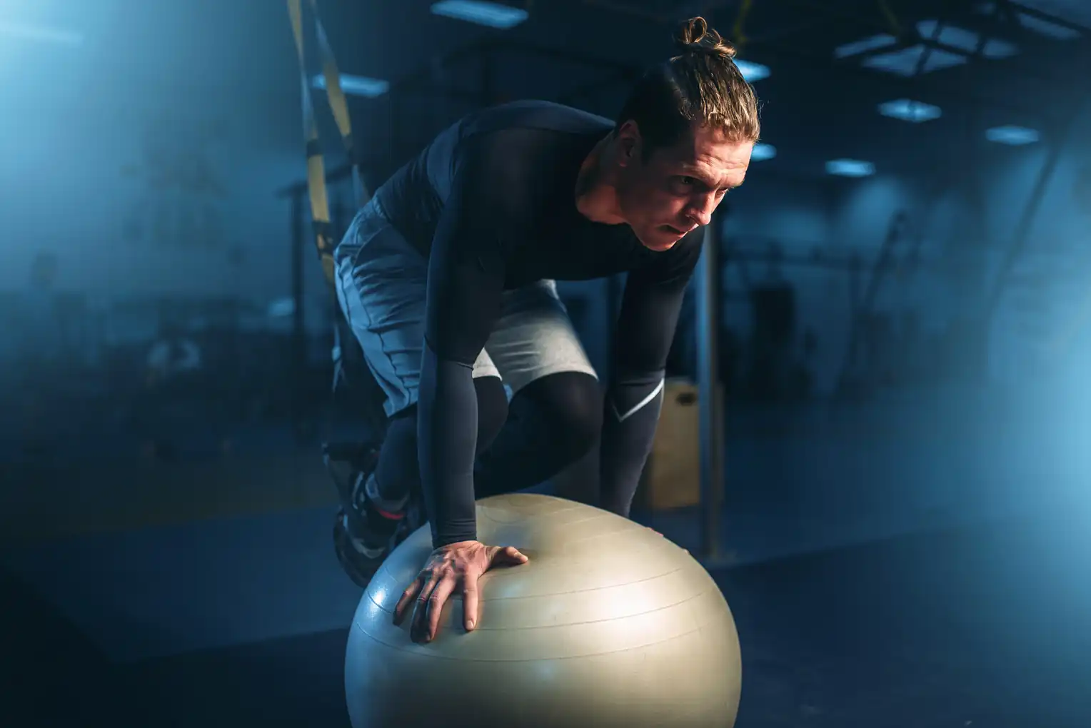 An athletic man performing an advanced core stability exercise using suspension straps and a Swiss exercise ball