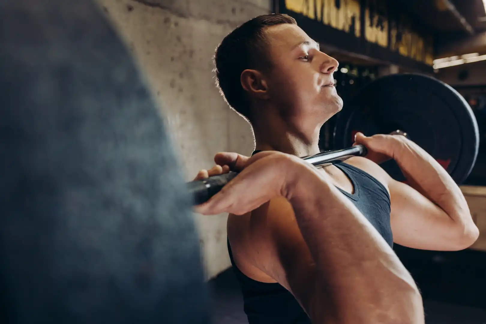 A young athletic man holding a weighted barbell in the front rack position during a workout