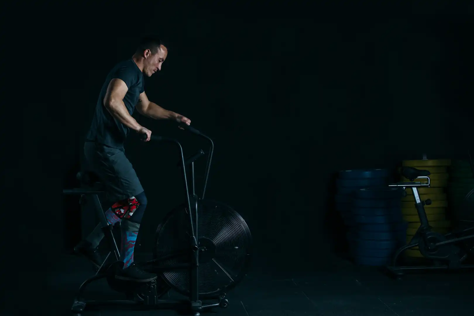 Athletic man performing high-intensity cardio training on a fan bike, representing HIIT workouts, endurance conditioning, and physical rehabilitation fitness.