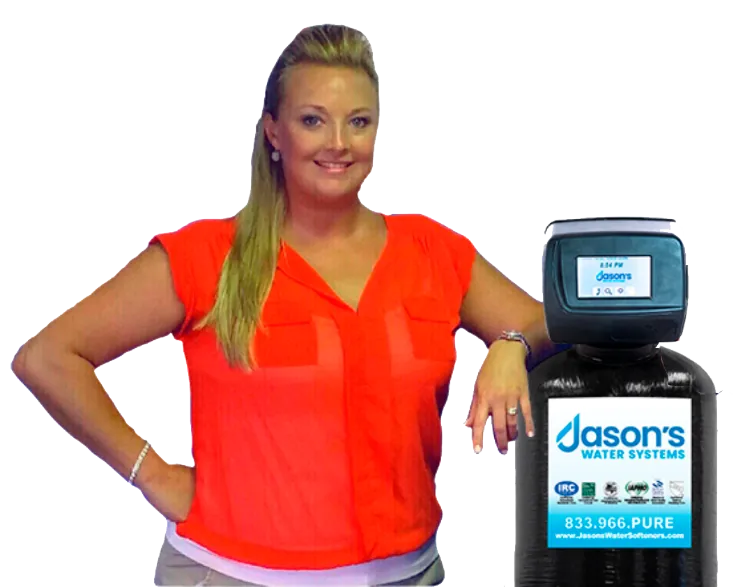 Woman in a red blouse standing with one hand on her hip and the other resting on a Jason’s Water Systems unit, with a dark background.