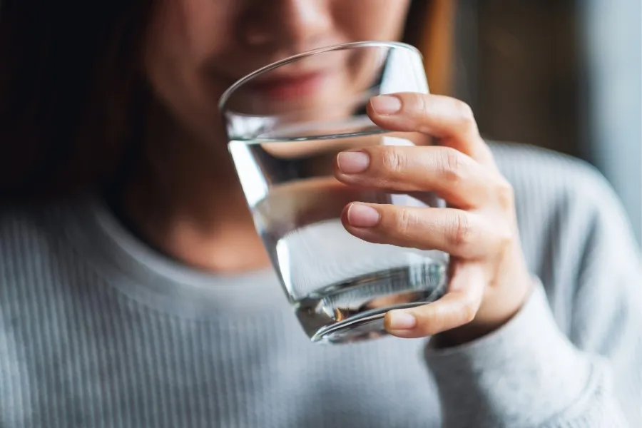 Person holding a clear glass of water close to their mouth.