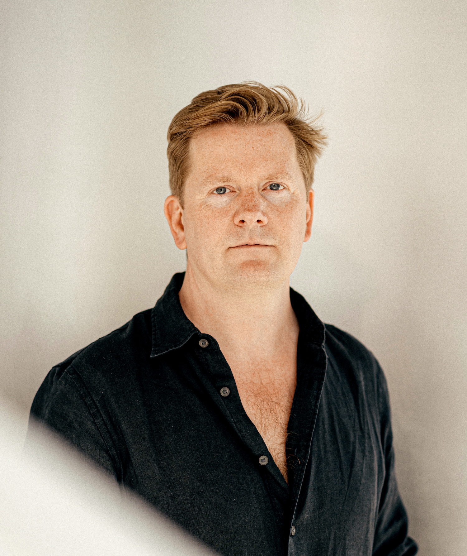 David Thulstrup wearing a black shirt looking into the camera with a light background behind him.
