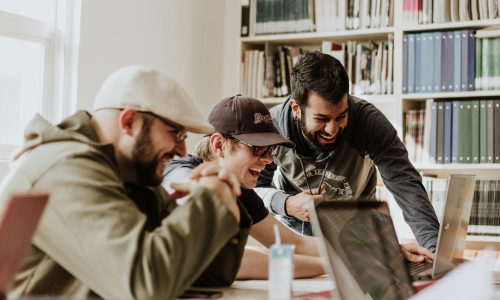 Group of working standing around laptop and laughing