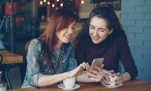 To young women pointing at mobile on table