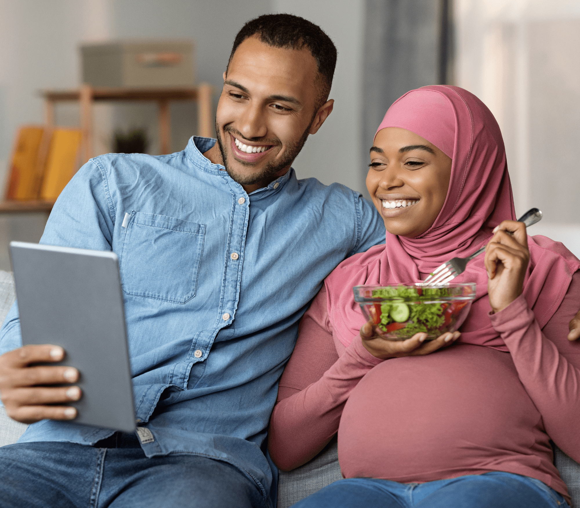 expecting couple with wife holding a bowl of salad and husband holding a tablet for a video call together