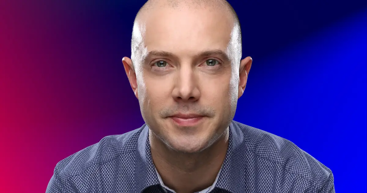 A person with a shaved head wearing a patterned shirt, set against a gradient background of blue and pink.