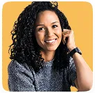 Smiling young woman with curly hair wearing a gray sweater against an orange background.