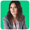 Confident woman with shoulder-length brown hair wearing a gray blazer, posing against a green background.