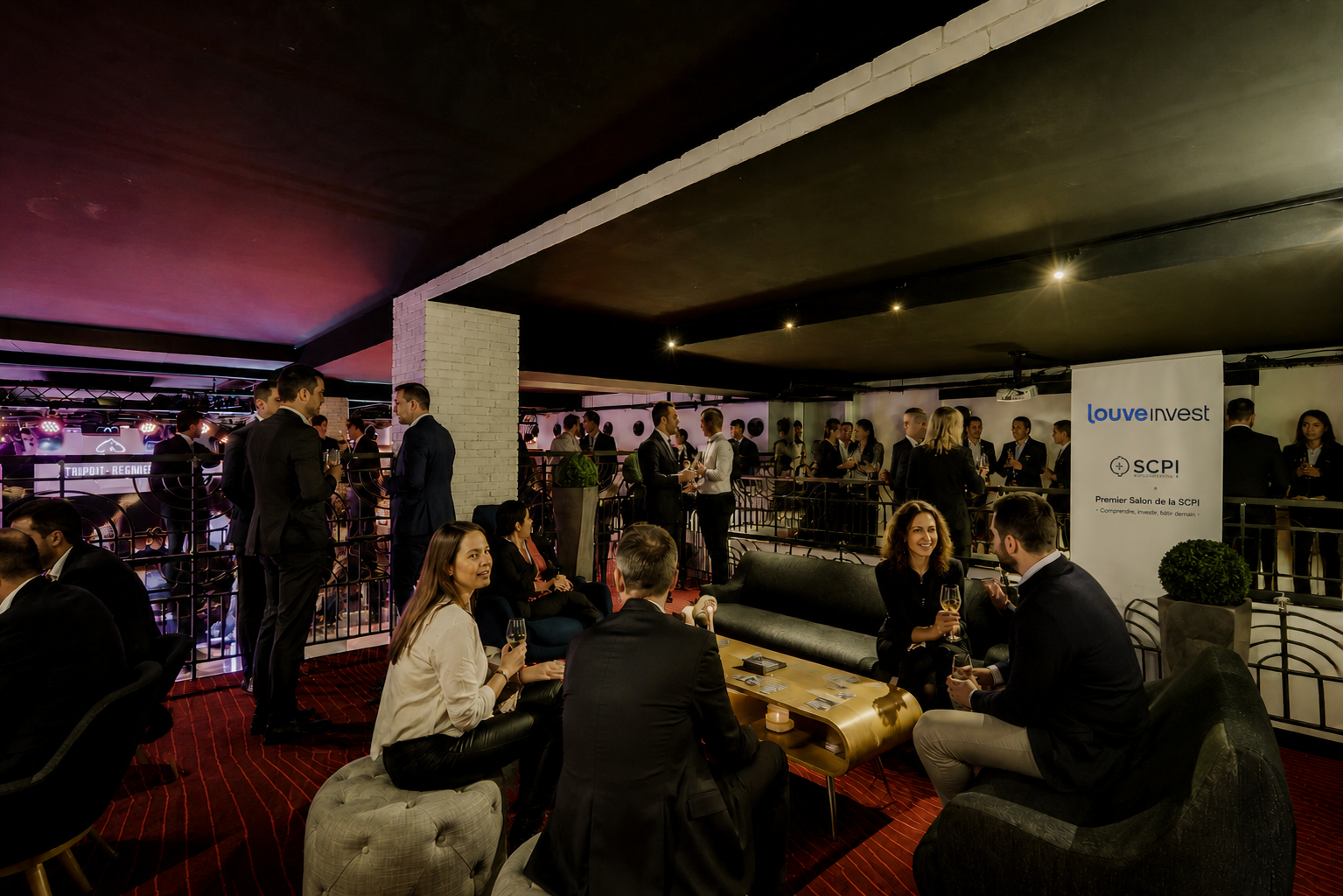 People networking and conversing at an indoor investment conference with Louve Invest banner visible.