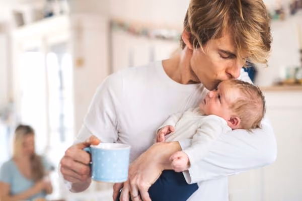 Young father holds his baby in the kitchen