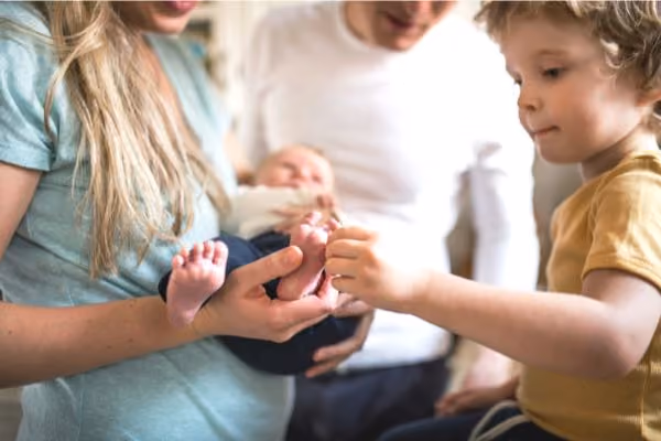 Mother and father show a toddler the newborn child