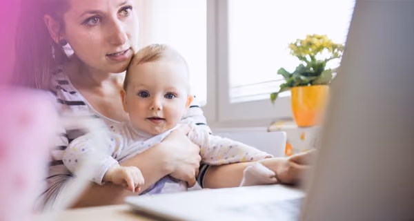Young mother with her baby on her lap doing research on her laptop