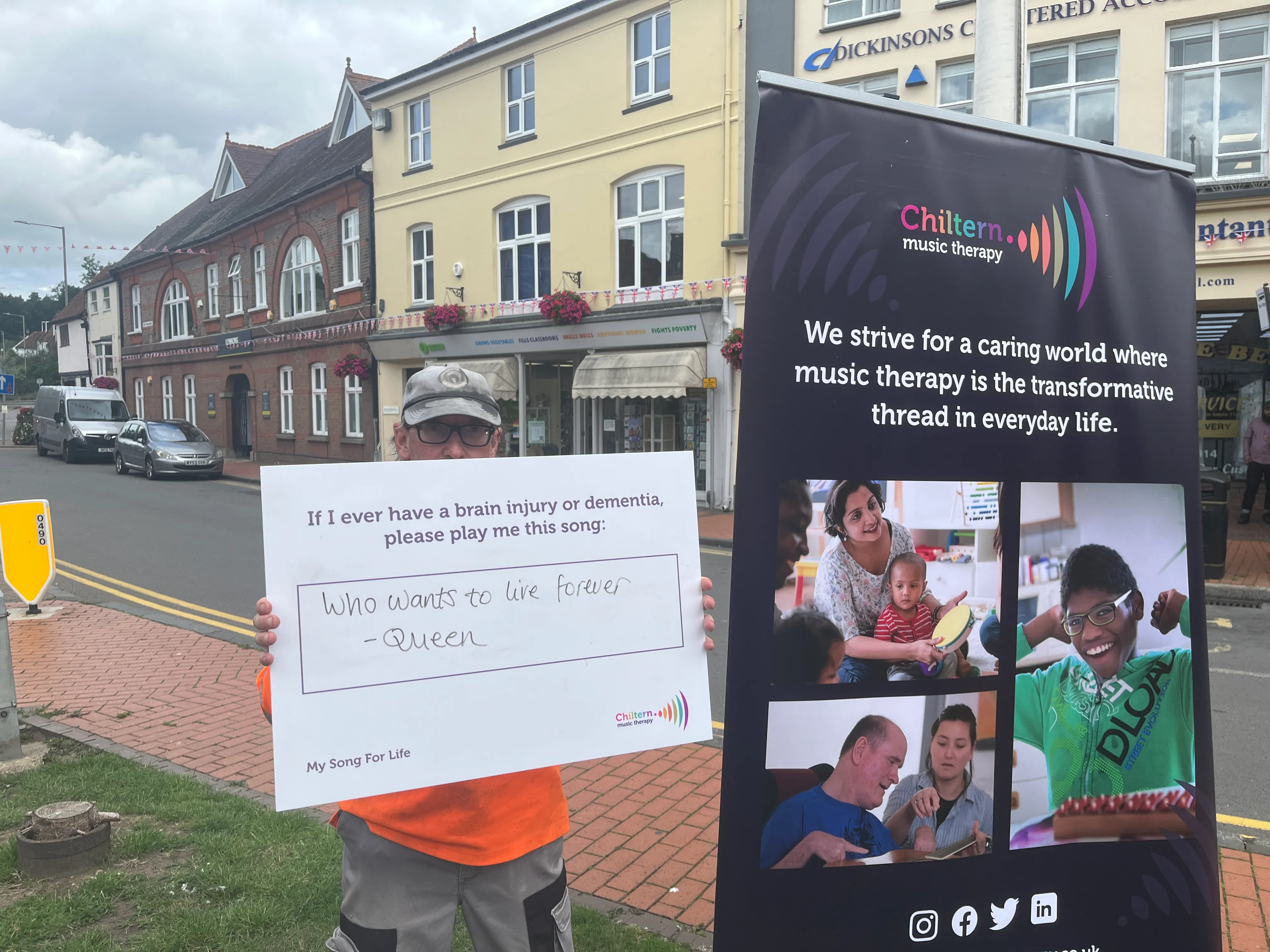 Image is of a man holding a sign that says "If I ever have a brain injury or dementia, please play me this song", underneath in handwriting it says "Who wants to live forever - Queen"