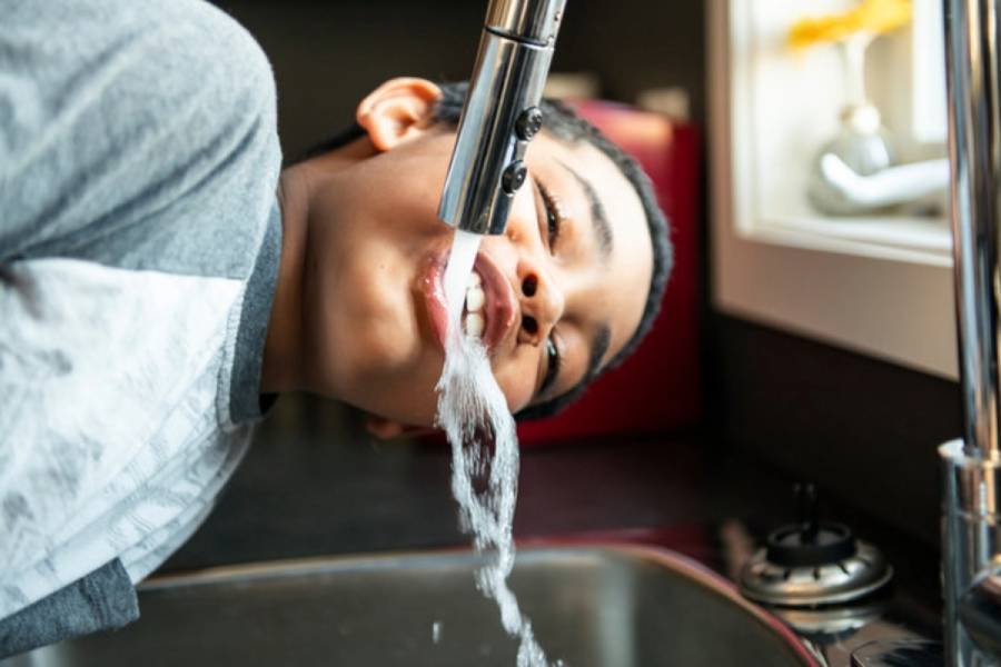 Boy drinking water from kitchen faucet
