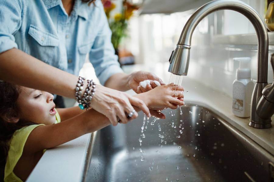 Mother helping child wash hands at kitchen sink