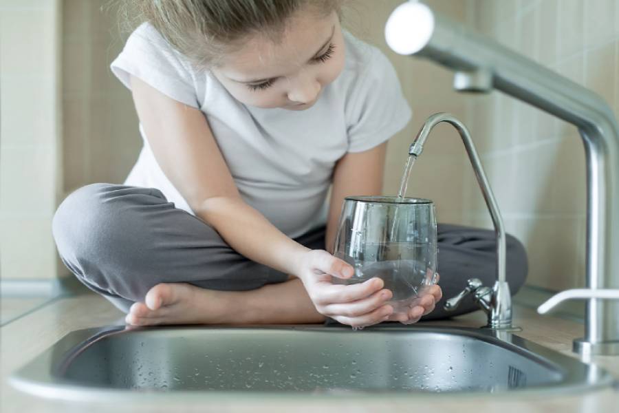 Child filling glass with water at sink