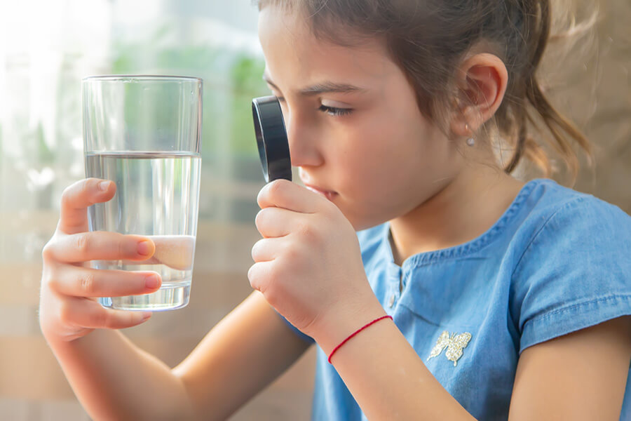 Girl examining glass of water with magnifying glass