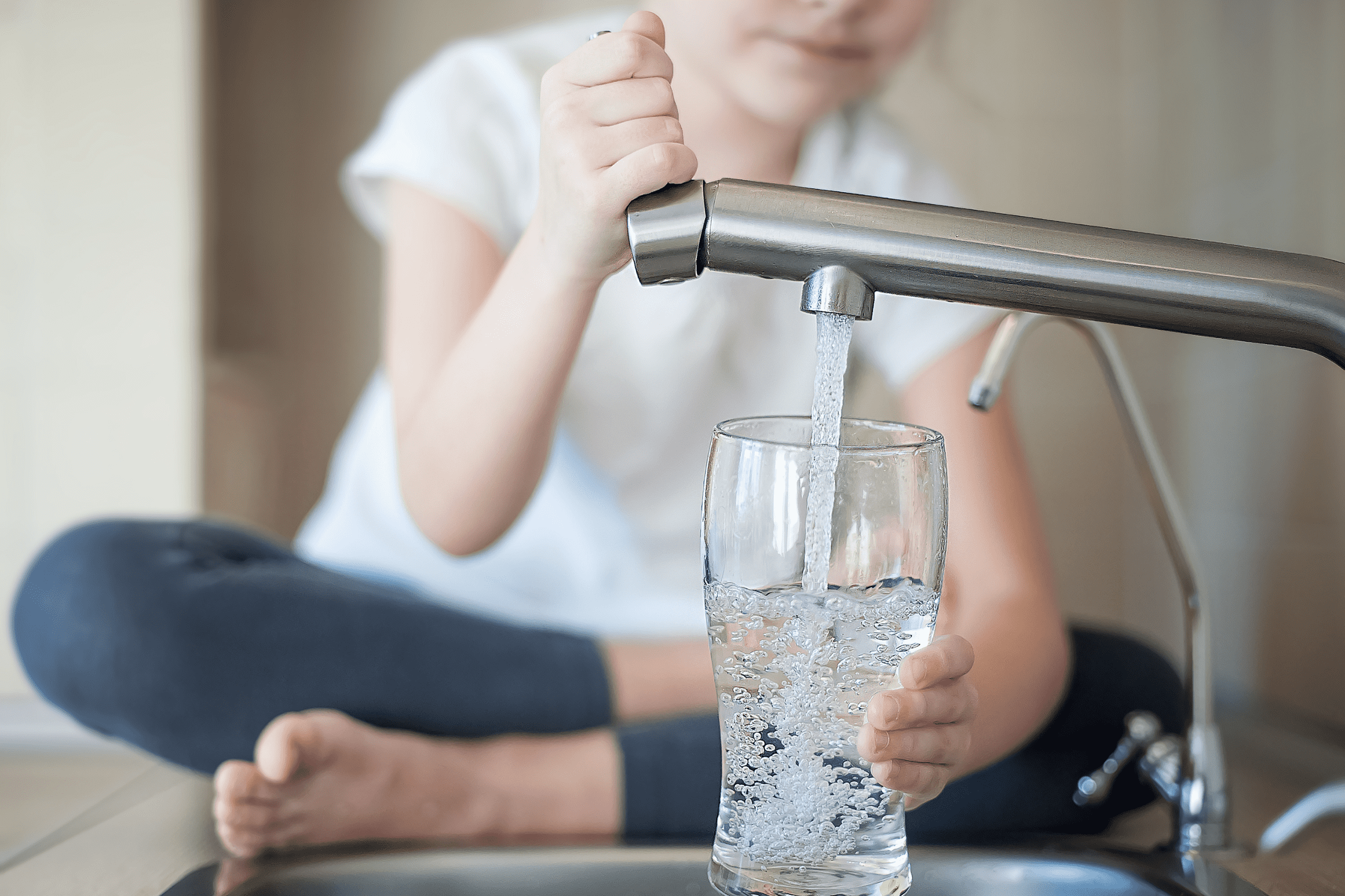 Child filling glass with water at sink