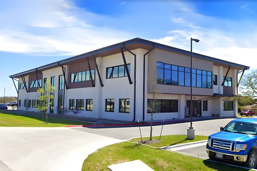 ChatGPT said:
A two-story medical office building with large windows, modern architectural design, and metal awnings, with a few cars parked in front and a clear blue sky overhead.
