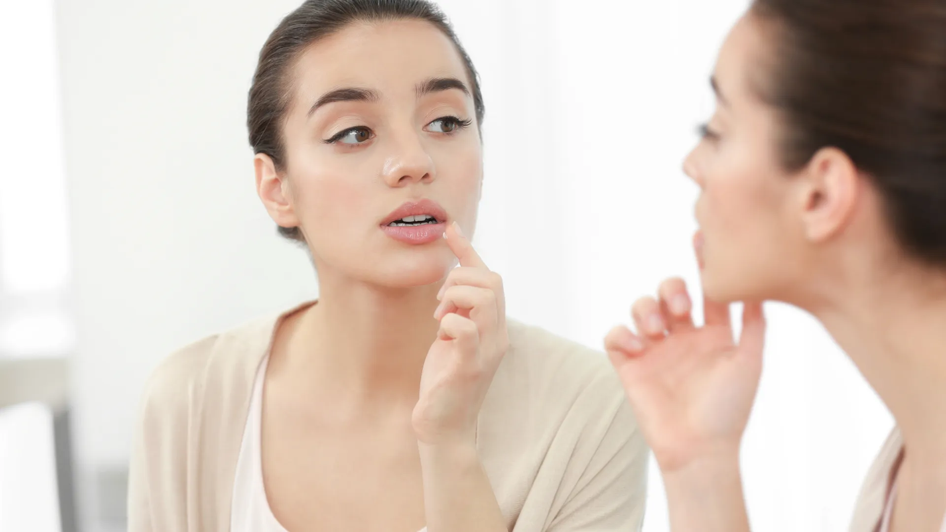 Woman applying lip balm while looking in the mirror, focused on skincare and beauty routine.