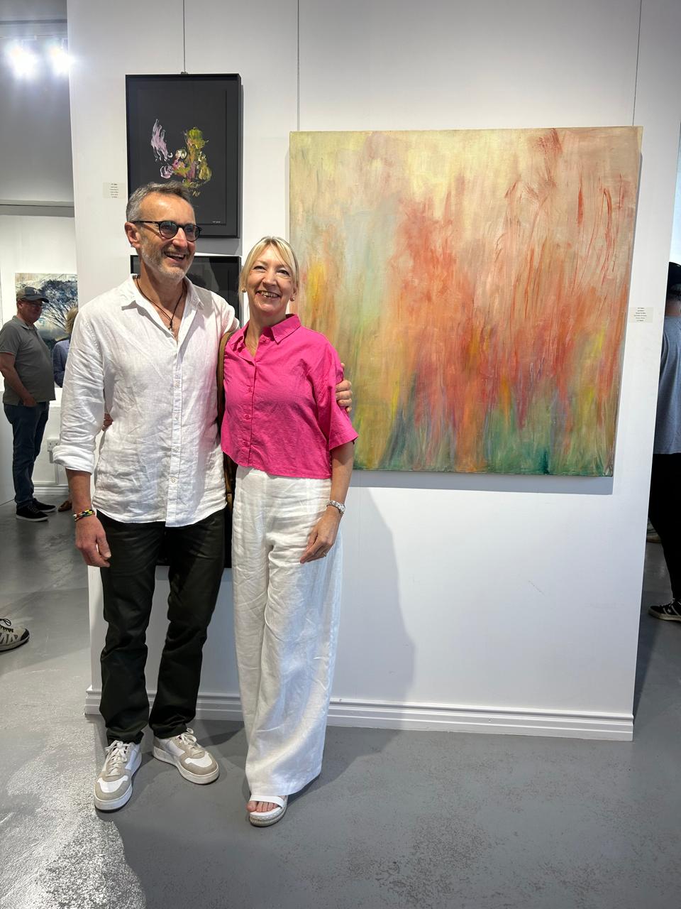 Jane with husband Al in AITY Gallery with one of her paintings
