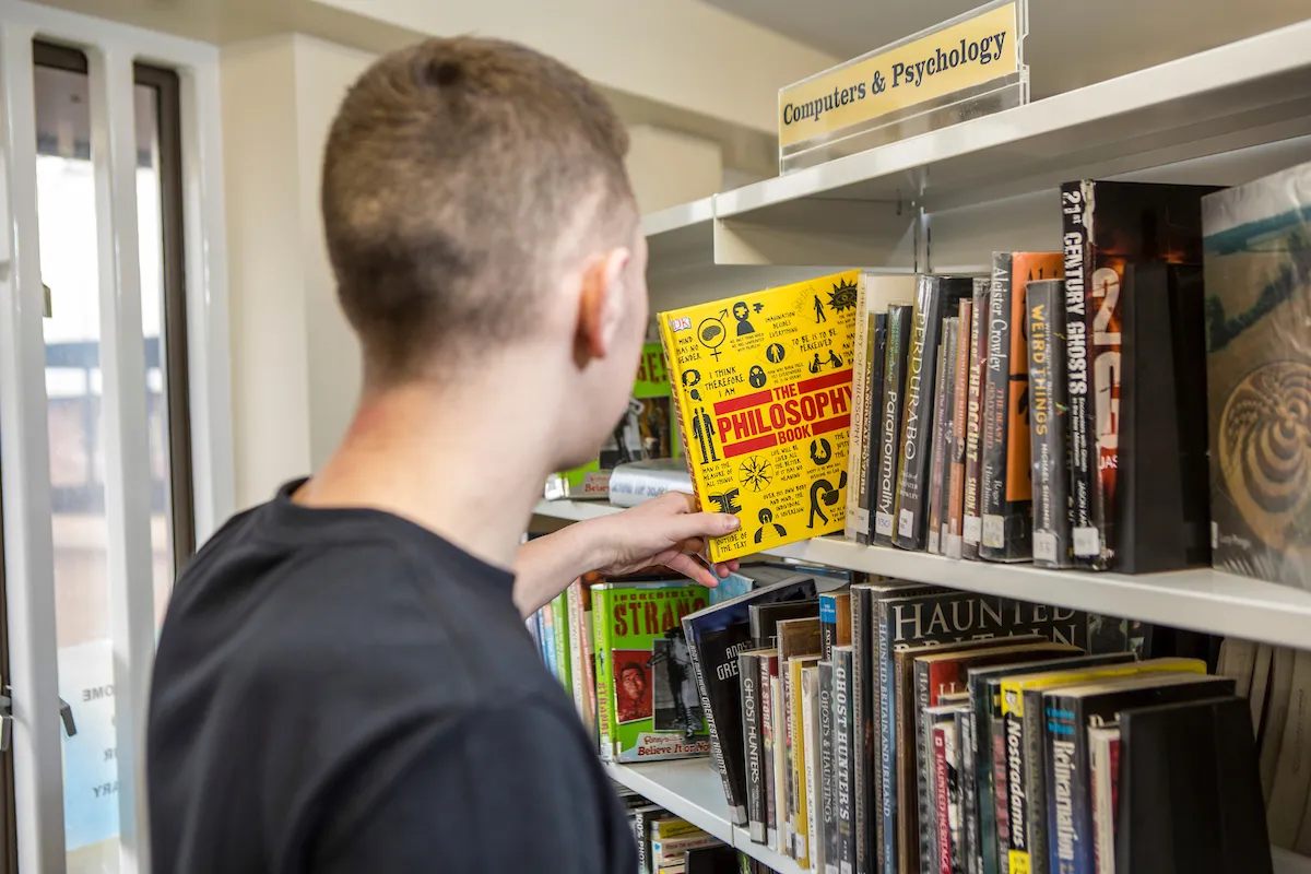 A person reaching for a book on a shelf in the prison library.