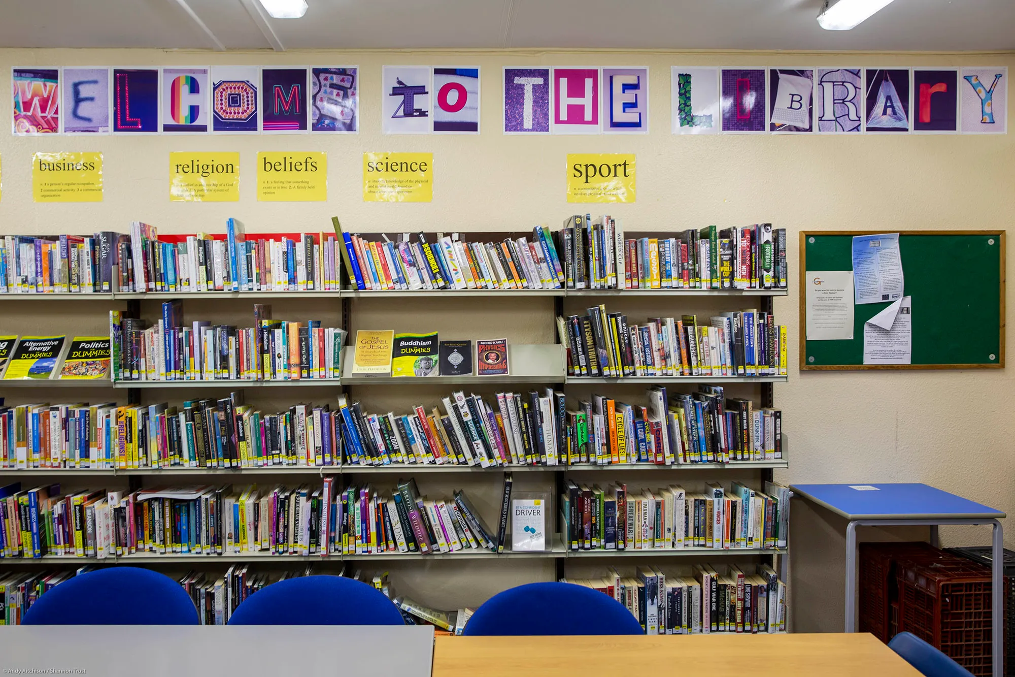 Shelves full of books in the prison library, with 'welcome to the library' spelled out on the wall above them.