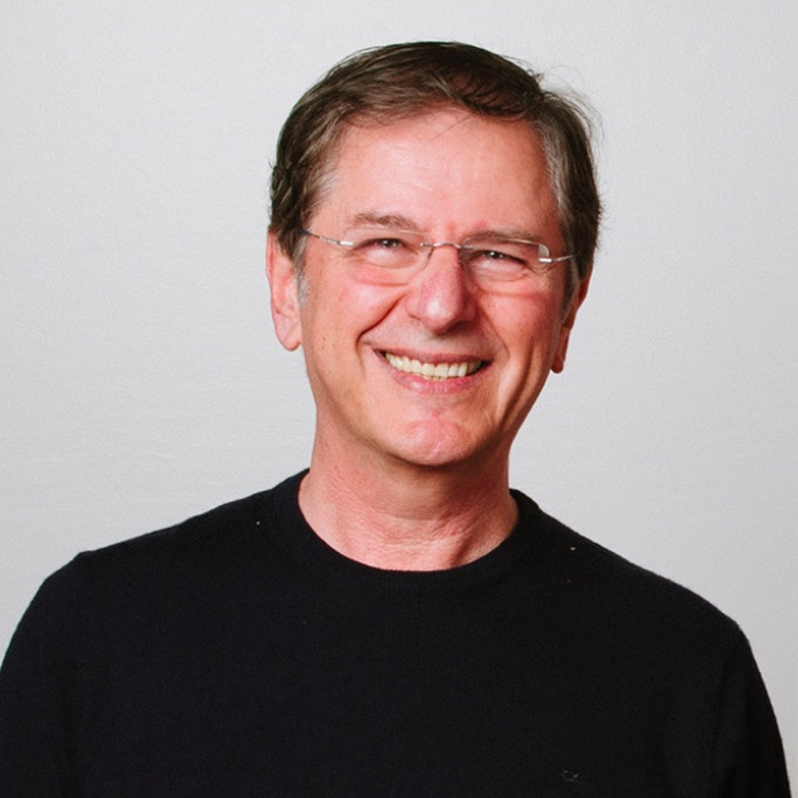 Smiling middle-aged man with short brown hair and glasses wearing a black shirt against a plain light background.