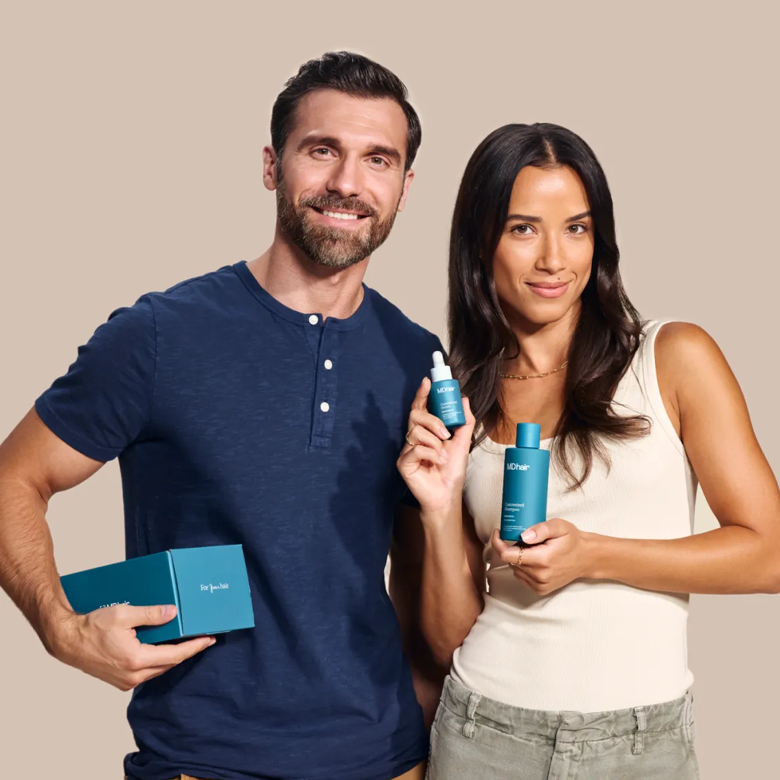 Smiling man in a navy blue shirt and woman in a white tank top holding MDhair customized shampoo products against a beige background.