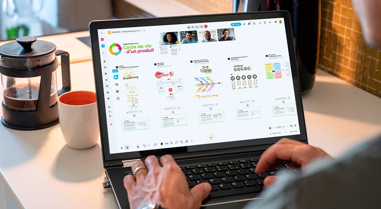 Une personne travaillant sur un ordinateur qui affiche un Board utilisant le template tout-en-un “Cycle de vie d’un produit”, avec d’autres personnes connectées en visio. | Klaxoon