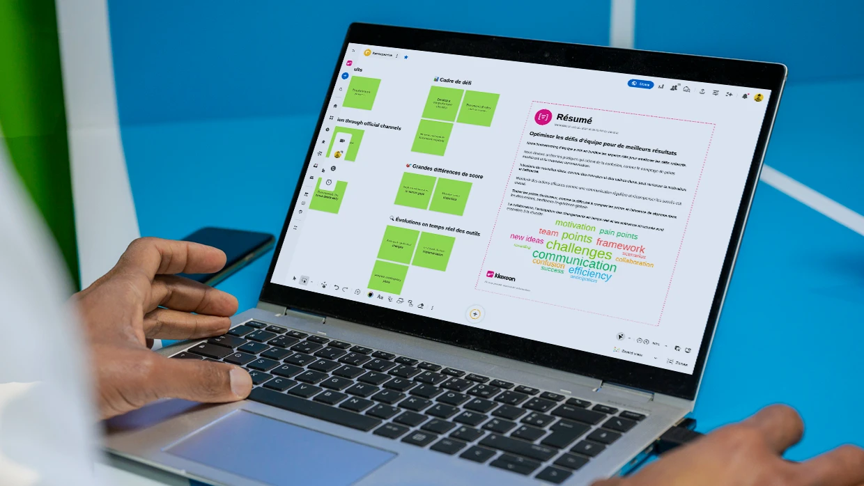 Une personne travaillant sur un ordinateur qui affiche un Board sur lequel les idées partagées sont résumées sous forme de texte et de nuage de mots via l’IA. | Klaxoon