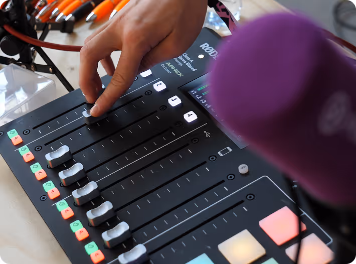 Hand adjusting a slider on an audio mixer next to a purple microphone cover.