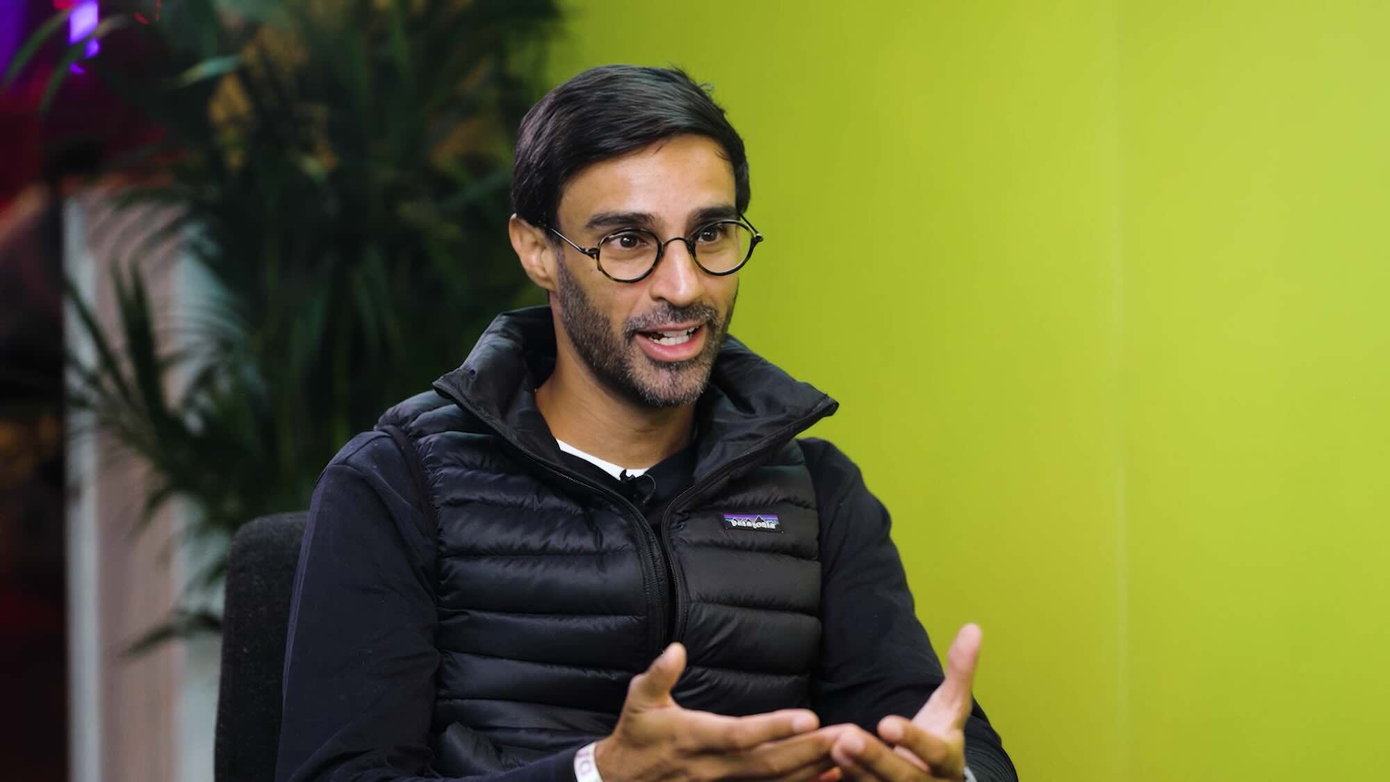 A man wearing glasses chatting with a green background.
