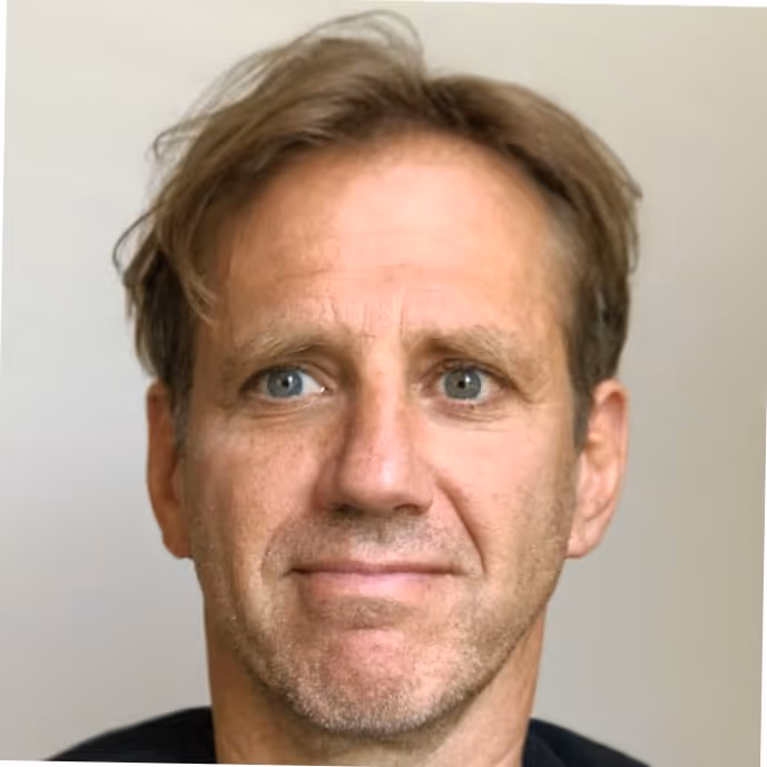 Close-up portrait of a middle-aged man with light brown hair and blue eyes against a plain background.