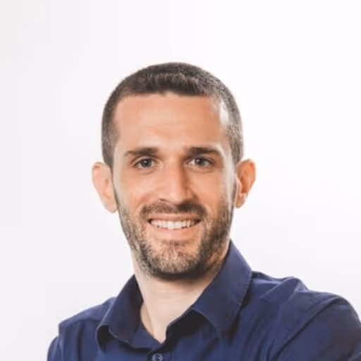 Portrait of a smiling man with short dark hair and a beard wearing a dark blue shirt.