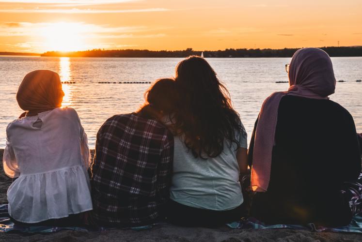 Four students lean against each other and watch the sunset over a lake.