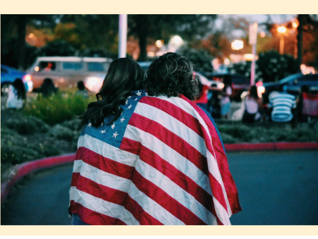 Two people wrapped in an American flag stand close together.