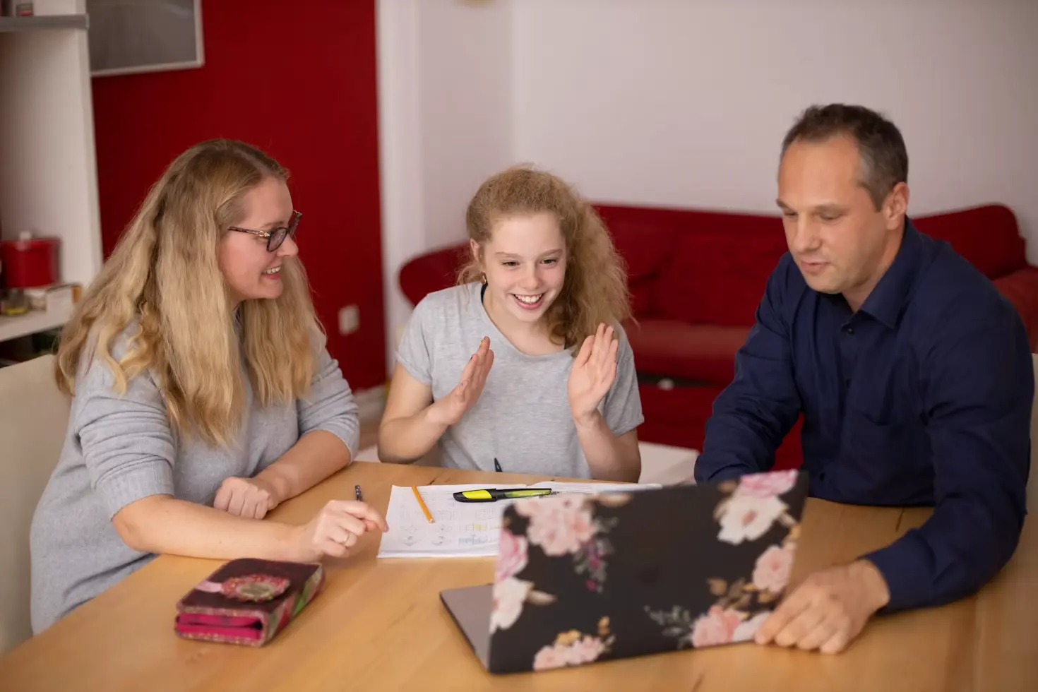 An exchange student and their host parents sitting together at a table with a laptop