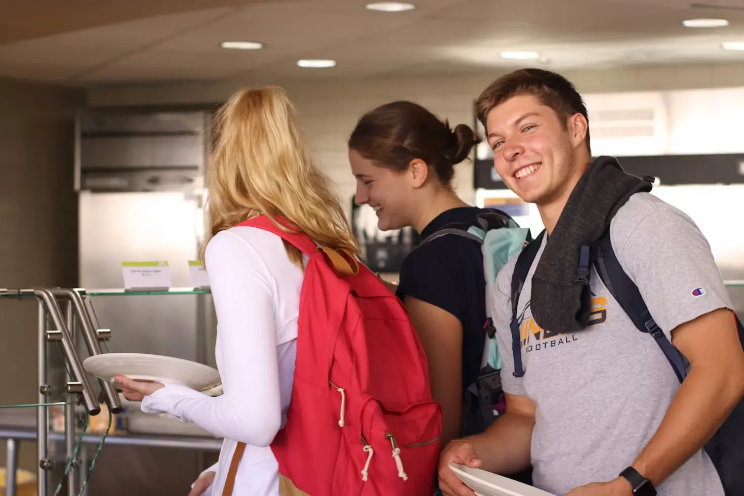 High school exchange students wearing backpacks holding lunch plates