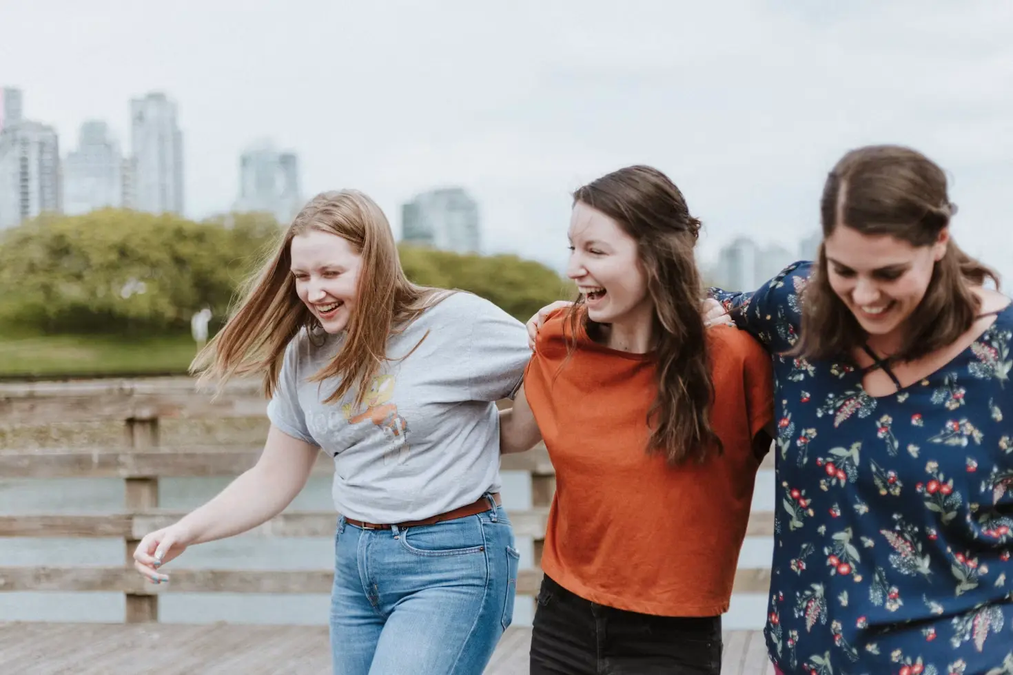 Three teenage friends outdoors laughing together with linked arms