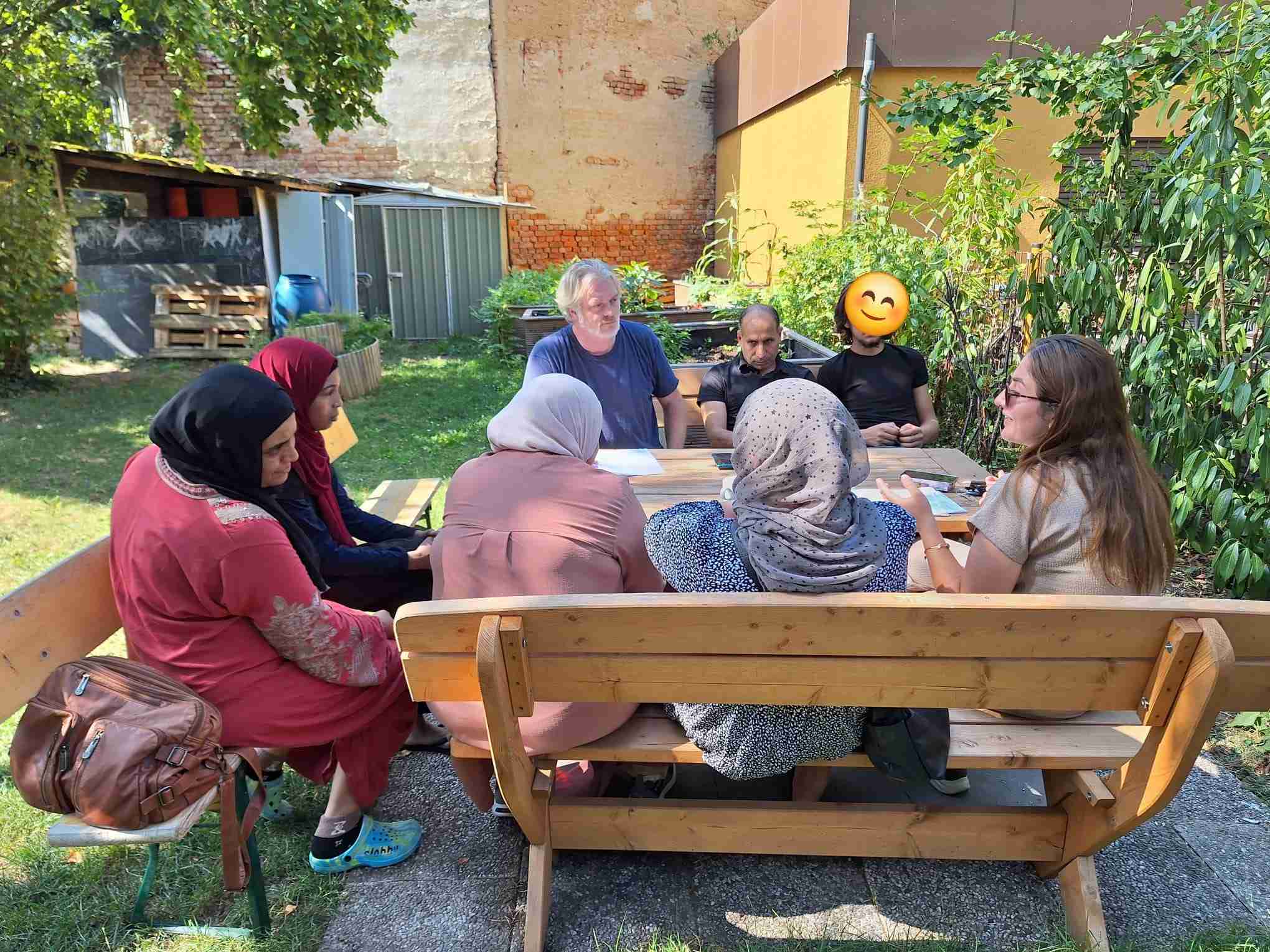 Gruppe von acht Personen sitzt im Freien an einem Holztisch und unterhält sich.