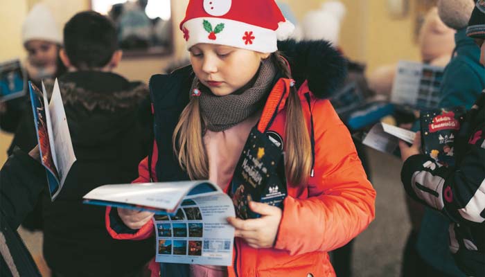 Ein Mädchen hält die Kalender von Licht im Osten in den Händen. Landschaftsbilder und Bibelverse.