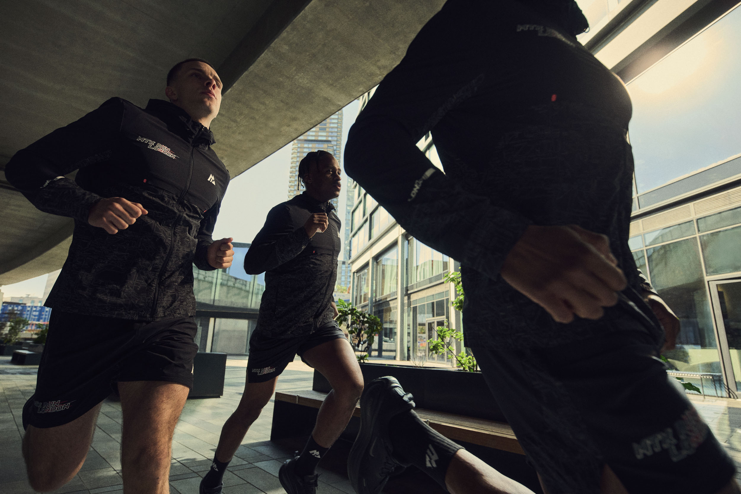 Three runners in black Montirex sportswear running through an urban East London walkway.