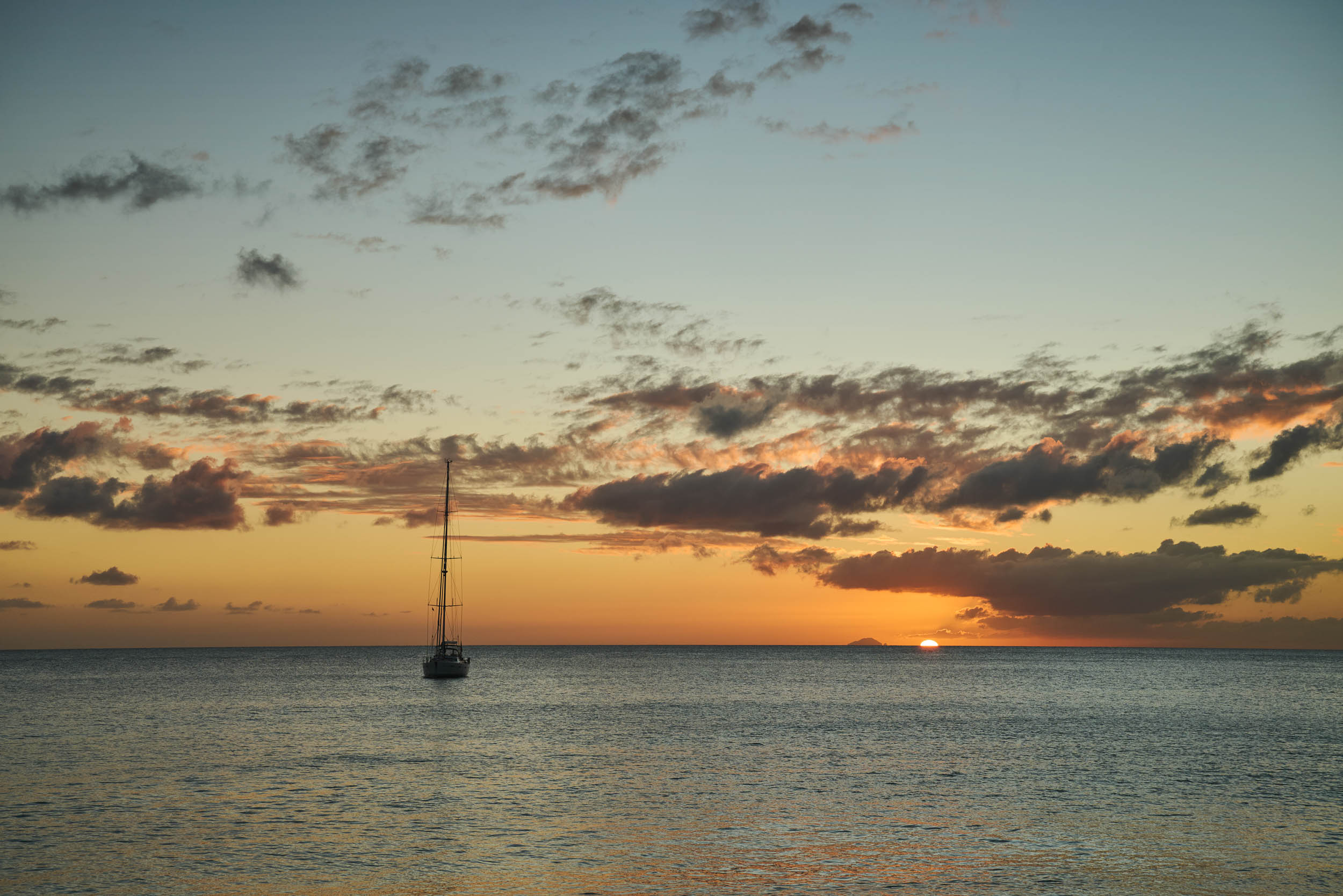 Sailboat anchored at sunset beneath a warm Caribbean sky