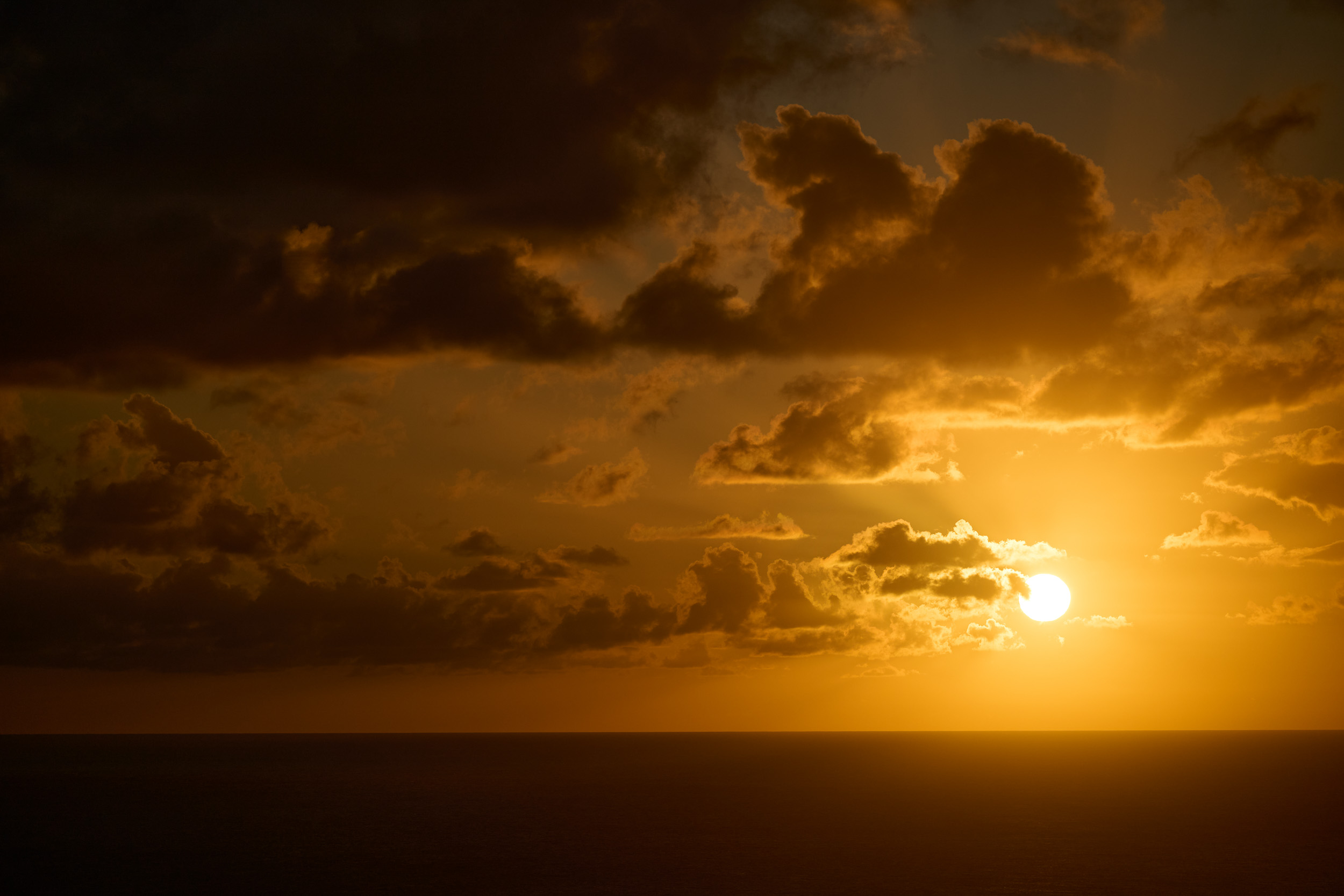Golden sun setting over the open sea and clouded horizon