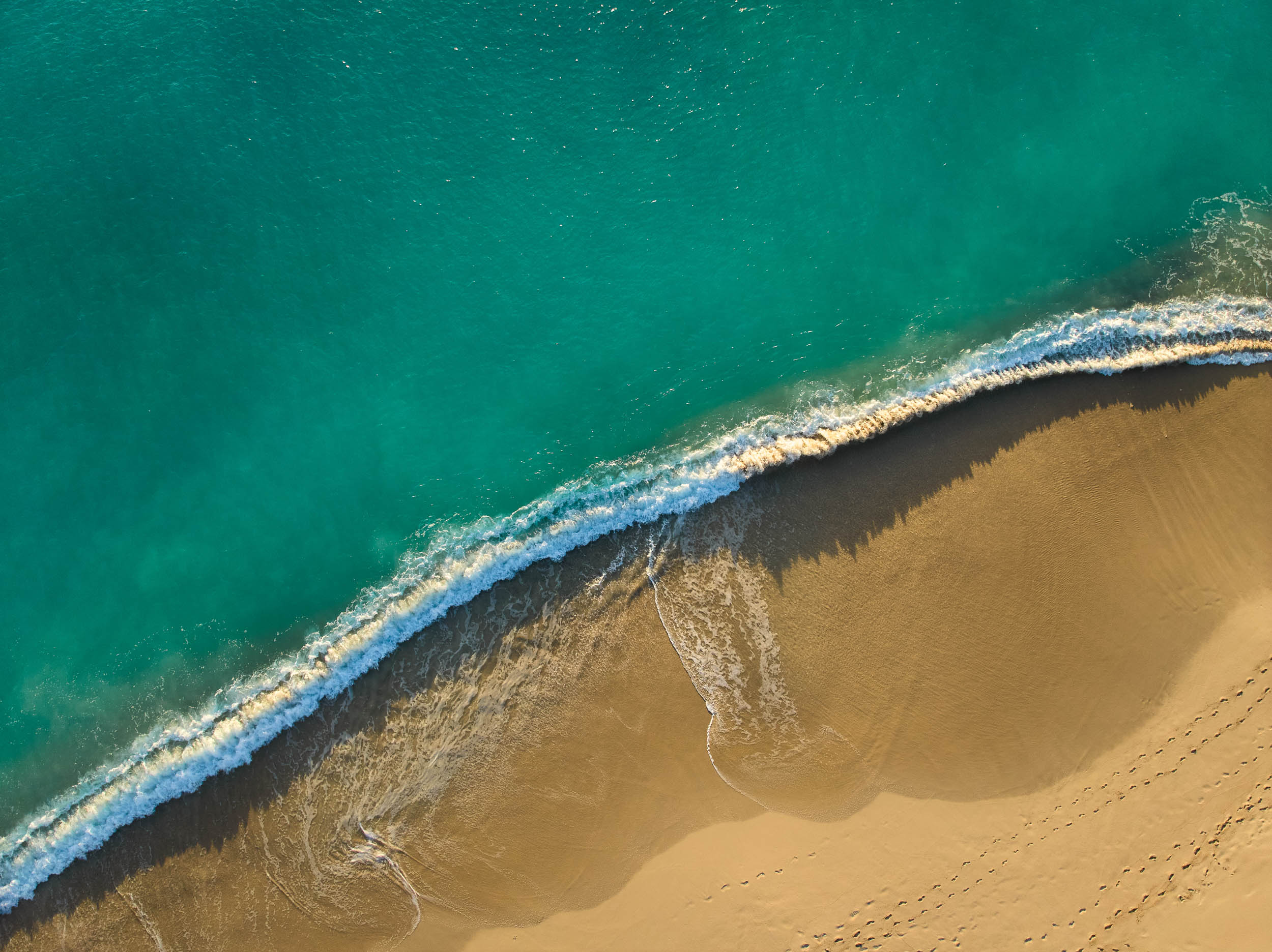 Aerial shoreline with turquoise water, white surf and golden sand
