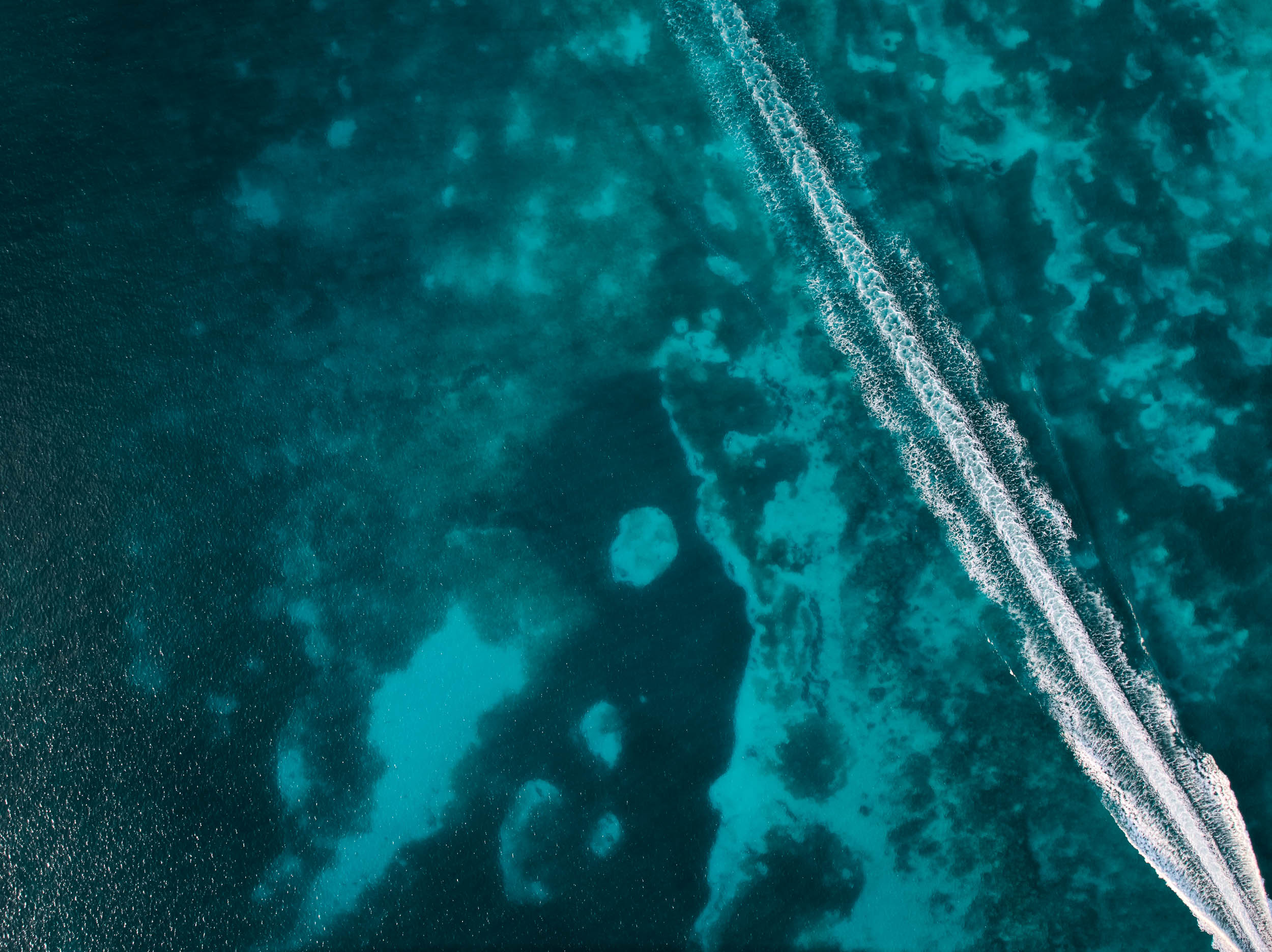 Arial view of boat wake cutting across deep blue Caribbean water and reef
